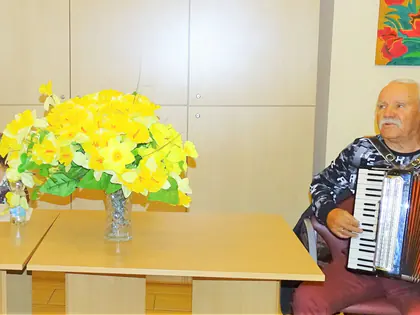Akordeonista gra przy stole z żółtymi kwiatami, obok kobieta z mikrofonem