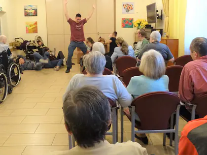 Mężczyzna tańczy przed mieszkańcami siedzącymi w świetlicy