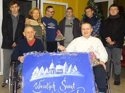 Młodzież i mieszkańcy na wózkach z kartką z napisem Wesołych Świąt