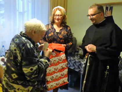 Kobieta i zakonnik wręczają mieszkance świąteczną torbę