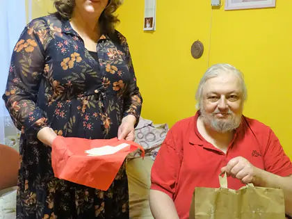 Pracownica wręcza mieszkańcowi w czerwonej koszulce papierową torbę