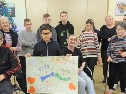 Mieszkańcy i młodzież pozują z plakatem z sercami przy choince