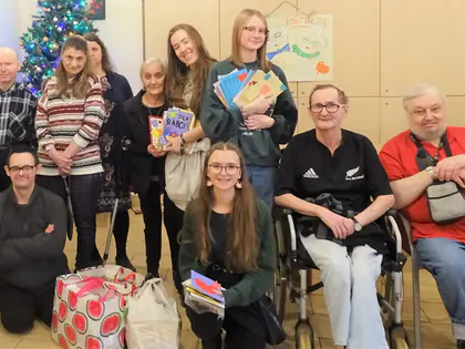 Mieszkańcy i młodzież pozują przy choince z kartkami i prezentami