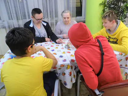 Młodzież i mieszkańcy grają w grę planszową przy stole z kolorowym obrusem