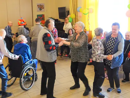 Pary tańczą w świetlicy, obok mieszkaniec na wózku