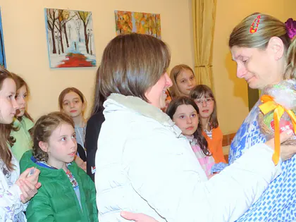 Kobieta przytula drugą z prezentem, obok stoją dziewczynki