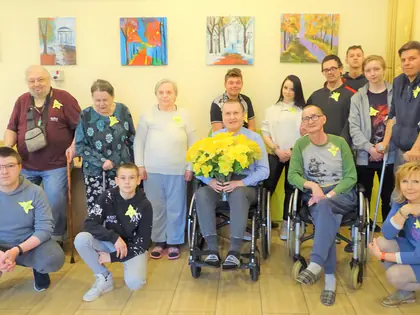 Młodzież i mieszkańcy z żółtymi papierowymi żonkilami przypiętymi do ubrań pozują z bukietem żonkili