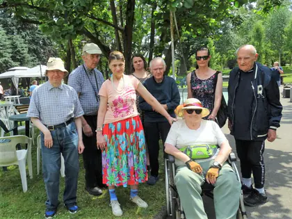 Mieszkańcy i opiekunki pozują na pikniku w parku, jedna mieszkanka na wózku