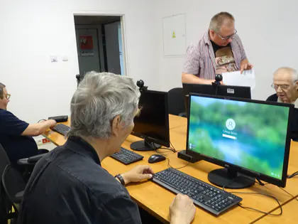 Seniorka pracuje przy komputerze, w tle prowadzący