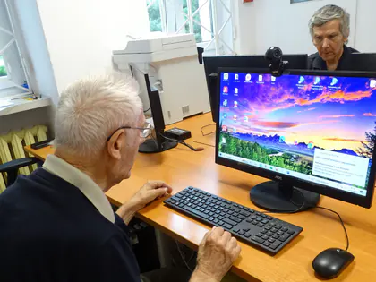 Senior siedzi przy komputerze z kolorową tapetą na ekranie