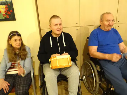Mieszkańcy siedzą w rzędzie, jeden trzyma bębenek