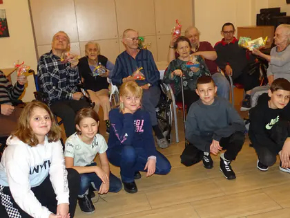 Dzieci kucają przed mieszkańcami trzymającymi świąteczne pierniki
