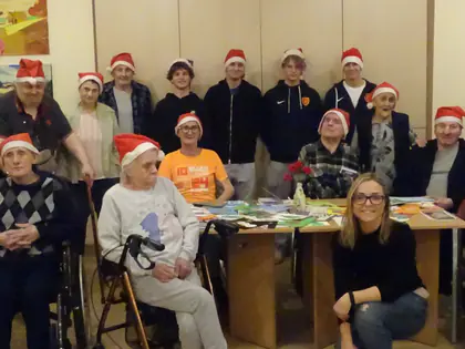 Mieszkańcy i goście w czapkach Mikołaja pozują w świetlicy