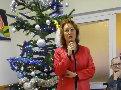 Kobieta w czerwonej kurtce mówi do mikrofonu przy choince