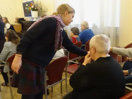 Uczennica w kraciastej spódnicy częstuje siedzących mieszkańców
