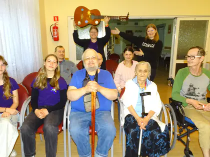 Harcerki z gitarą i mieszkańcy siedzą w rzędzie, jedna z harcerek trzyma gitarę nad głową