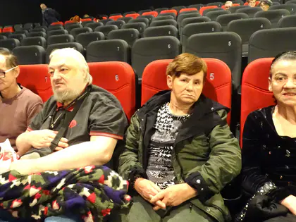 Czworo mieszkańców siedzi w kinie na czerwonych fotelach