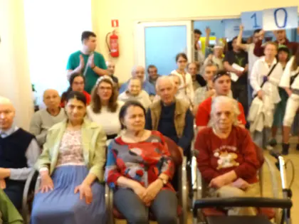 Mieszkańcy klaszczą w sali, za nimi młodzież z planszami z liczbami