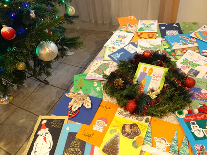 Kolorowe kartki świąteczne od uczniów rozłożone na stole obok stroika i choinki