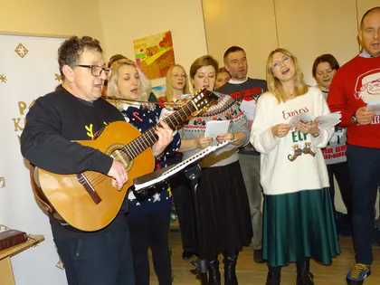 Grupa śpiewa kolędy z gitarą w świątecznych swetrach