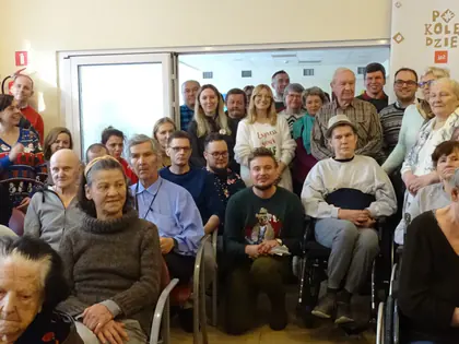 Duża grupa mieszkańców i gości pozuje w sali podczas wspólnego kolędowania
