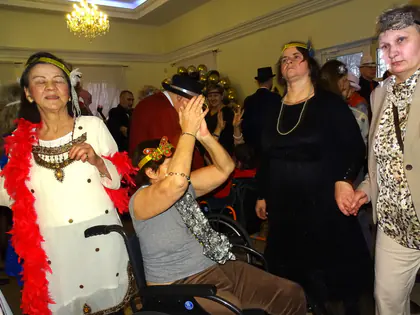 Uczestnicy balu przebrani w stylu lat dwudziestych, w boa i opaskach, tańczą w sali