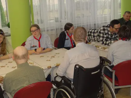 Skauci i mieszkańcy siedzą przy długim stole w jadalni
