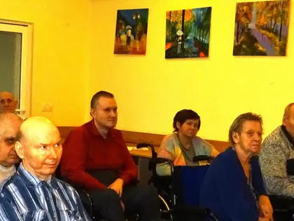 Mieszkańcy siedzą w sali w półokręgu i słuchają prelekcji, na pierwszym planie prowadząca