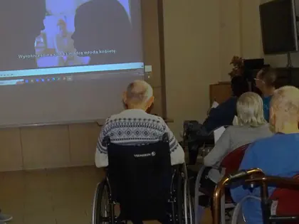 Mieszkańcy oglądają film wyświetlany na ekranie w sali