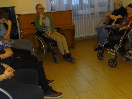 Młodzież siedzi obok mieszkańców na wózkach w sali z pianinem