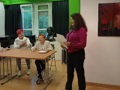 Prowadząca czyta przed mieszkankami siedzącymi przy stole