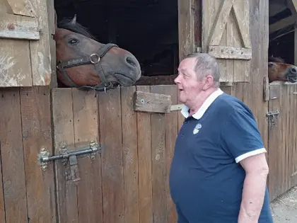 Mieszkaniec stoi przy stajni, z boksu wygląda koń