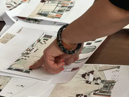 Dłoń wskazuje rysunki projektu wnętrza na kartkach rozłożonych na stole