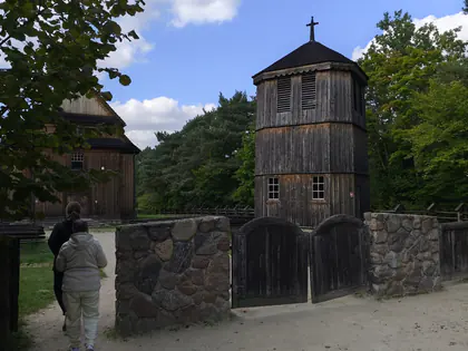 Drewniana dzwonnica w skansenie, przed nią idzie mieszkanka