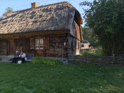 Mieszkańcy siedzą na ławce przed drewnianą chatą