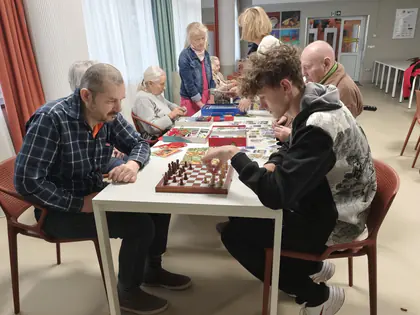 Mężczyzna i chłopak grają w szachy przy stole, w tle inni gracze