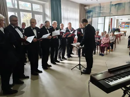 Chórzyści z teczkami śpiewają pod batutą dyrygenta