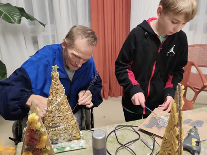 Chłopiec i mieszkaniec przyklejają ozdoby do kartonowej choinki