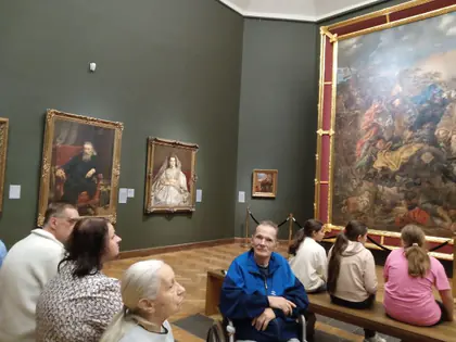 Grupa zwiedzających siedzi na ławce w sali muzeum z obrazami w złoconych ramach