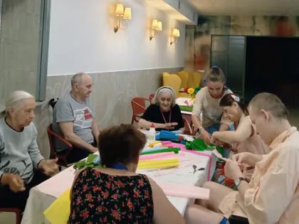 Uczestnicy warsztatów przy stole pełnym kolorowej bibuły
