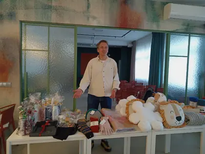 Mężczyzna stoi za stołami z paczkami darów, skarpetami i pluszowymi lwami