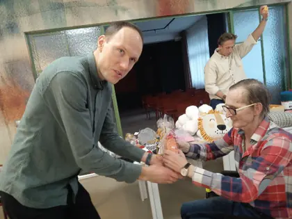 Mężczyzna wręcza nagrodę mieszkańcowi w kraciastej koszuli podczas bingo