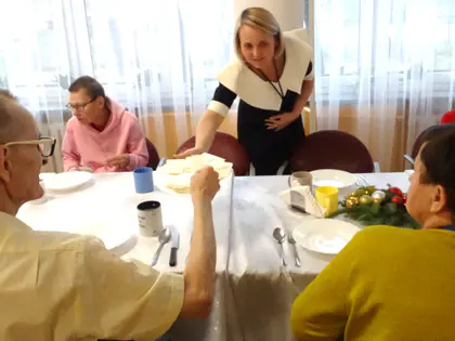 Mieszkańcy przy stole z opłatkami i świątecznym stroikiem, nad nimi pochyla się pracownica