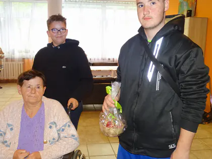 Mieszkanka na wózku z dwoma chłopcami, jeden trzyma pakunek z upominkiem