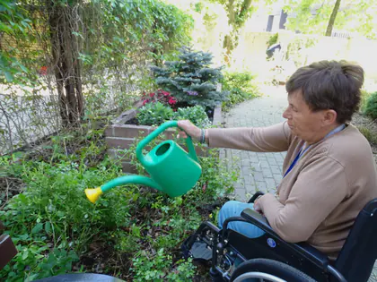Mieszkanka na wózku podlewa kwiaty zieloną konewką w ogrodzie