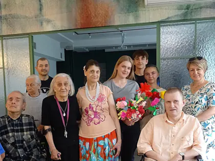 Mieszkańcy i młodzież pozują w grupie, jedna z kobiet trzyma bukiet kolorowych kwiatów