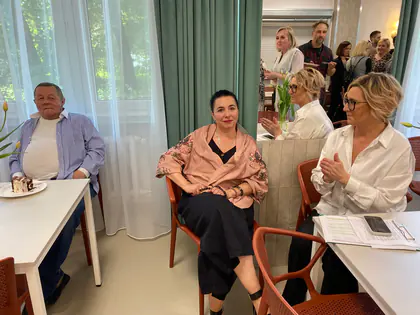 Goście siedzą przy stołach podczas uroczystości, jedna z kobiet klaszcze