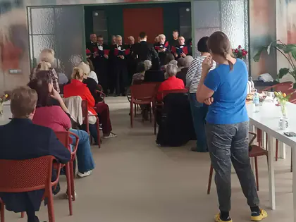Chór śpiewa w głębi świetlicy, mieszkańcy siedzą na krzesłach