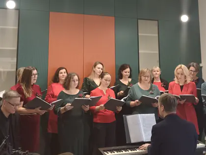 Chór w czerwieni i zieleni śpiewa ze skrzypkiem i pianistą