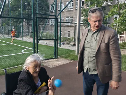 Mieszkanka na wózku z piłką, obok stoi mężczyzna
